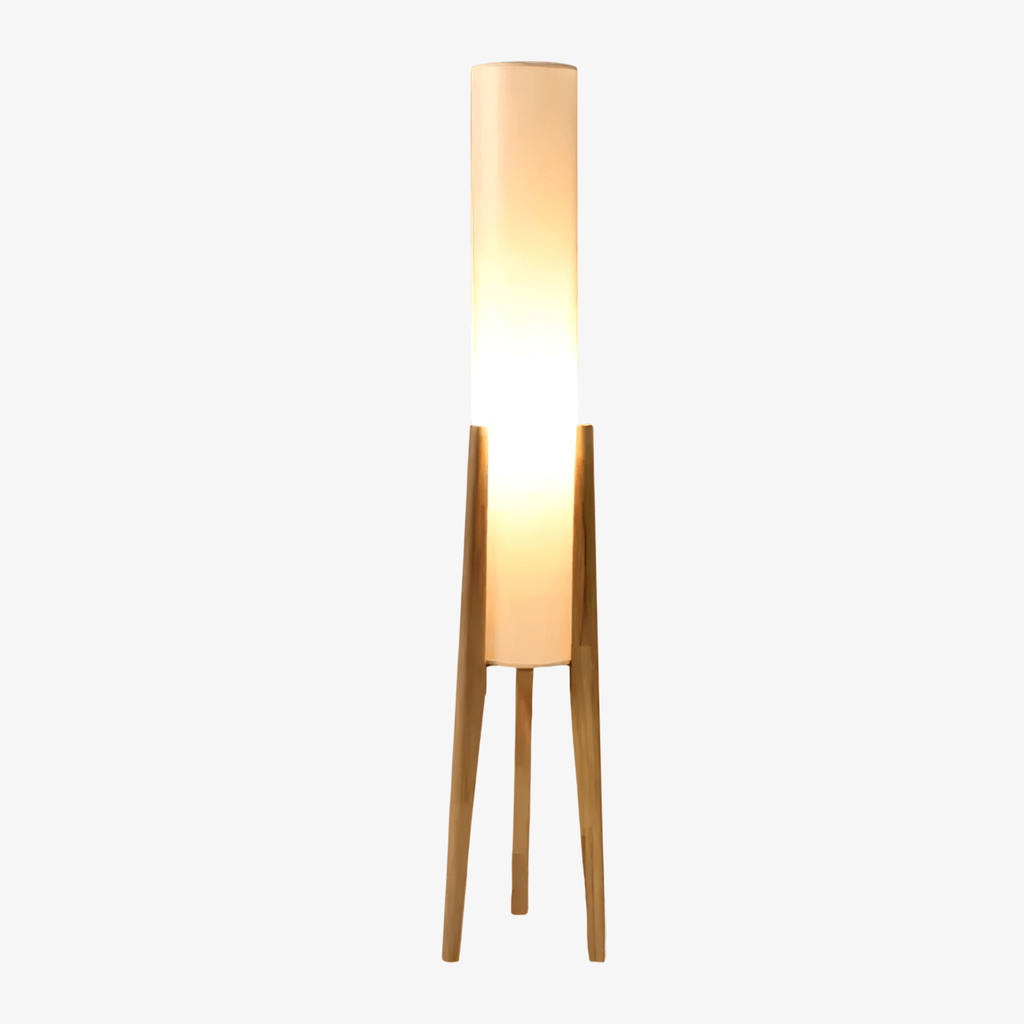 Clérachic floor lamp with a glowing white cylinder shade on three light wood legs, on a pale grey backdrop.