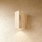 Clérachic wall lamp in rectangular pitted stone with a pale wood mounting base, uplight glowing below.