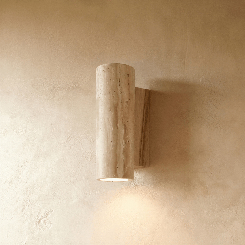Clérachic wall lamp in a round stone cylinder mounted on a pale-wood base plate, its downlight glowing softly below.