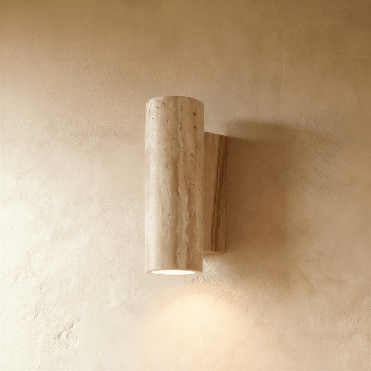 Clérachic wall lamp in a round stone cylinder mounted on a pale-wood base plate, its downlight glowing softly below.