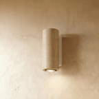Clérachic wall lamp in round pitted stone on a pale metal mounting base against a plaster wall.