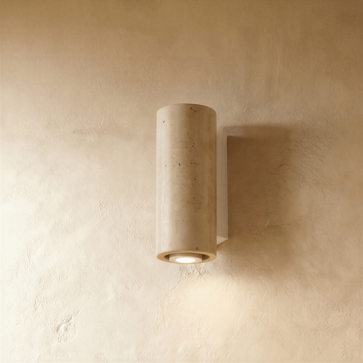 Clérachic wall lamp in round pitted stone on a pale metal mounting base against a plaster wall.