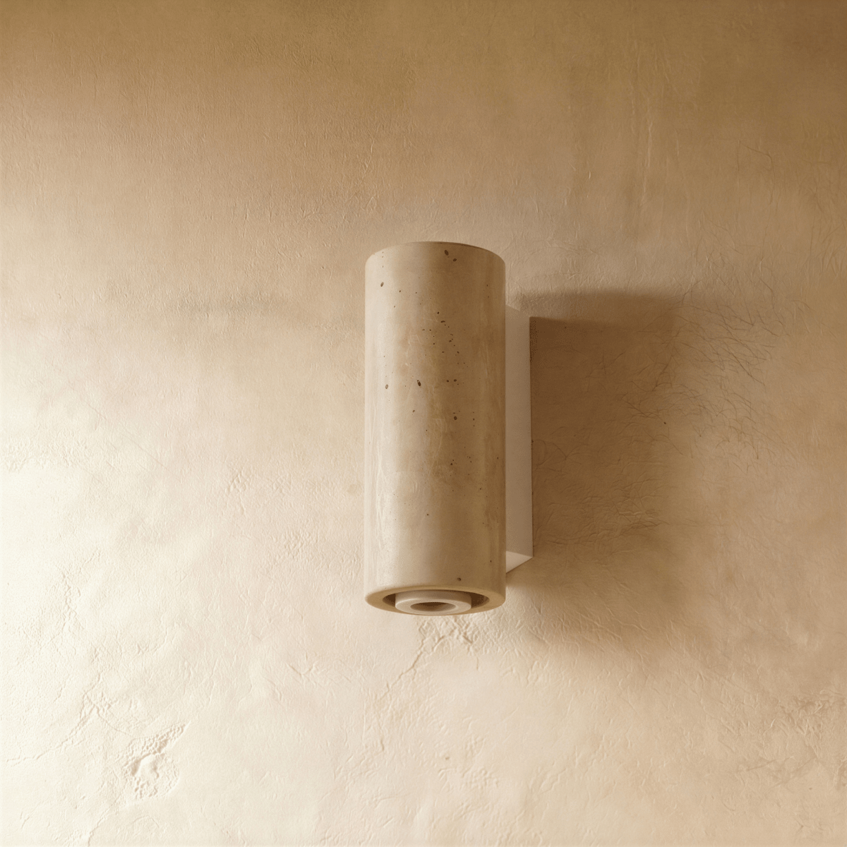 The Clérachic wall lamp's cylindrical stone shade with its pale metal base, lit from below.