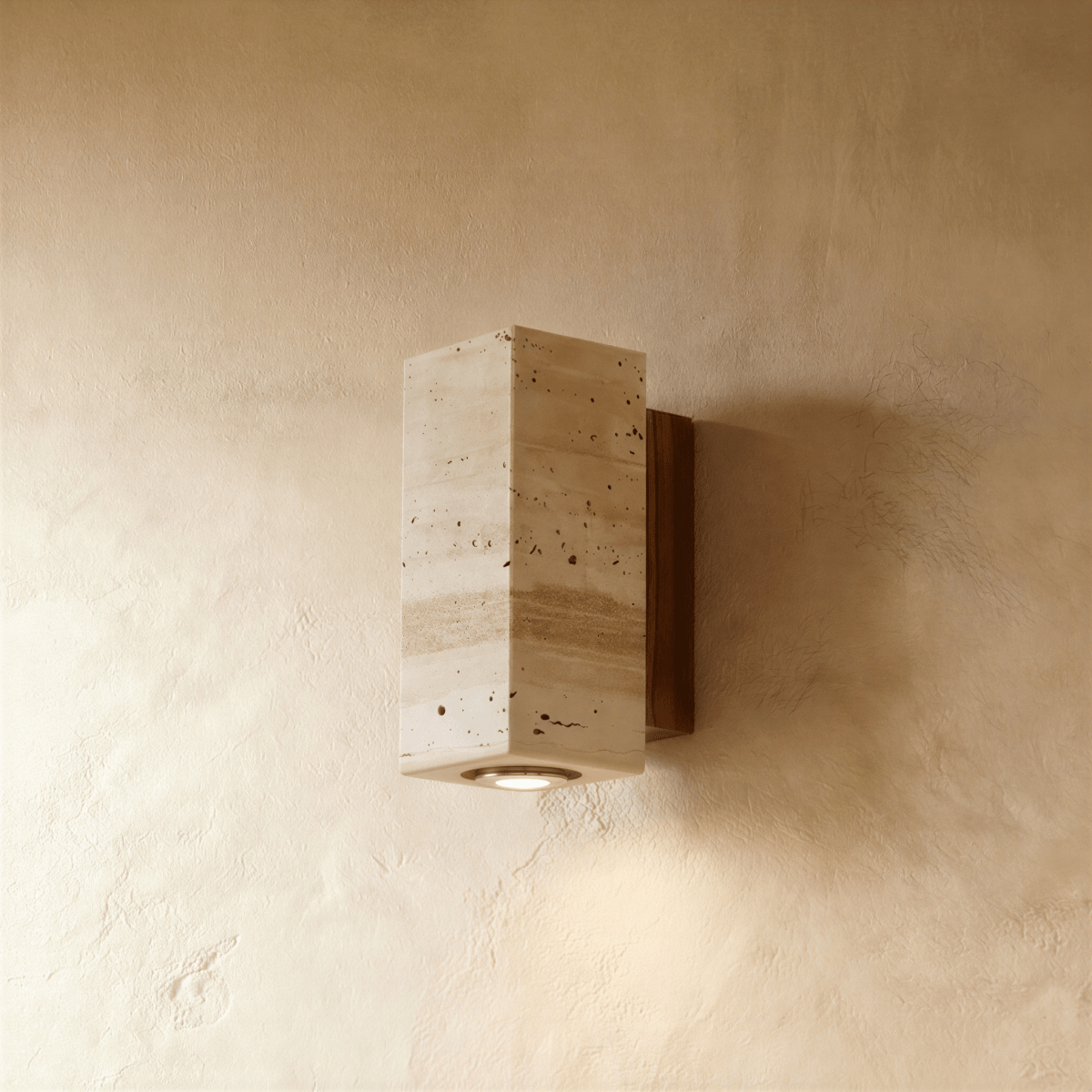 Clérachic wall lamp in rectangular pitted stone mounted on a dark walnut wood base, its downlight glowing on plaster.