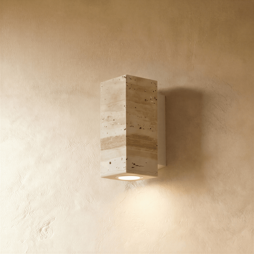 Clérachic wall lamp shown front-on in rectangular pitted travertine-look stone, its soft downlight glowing below.