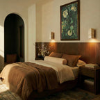 Two Clérachic wall lamps flank a dark wood headboard, lighting a warm-toned bedroom at dusk.