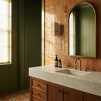A Clérachic wall lamp mounted on terracotta tile beside an arched mirror in a sunlit bathroom.