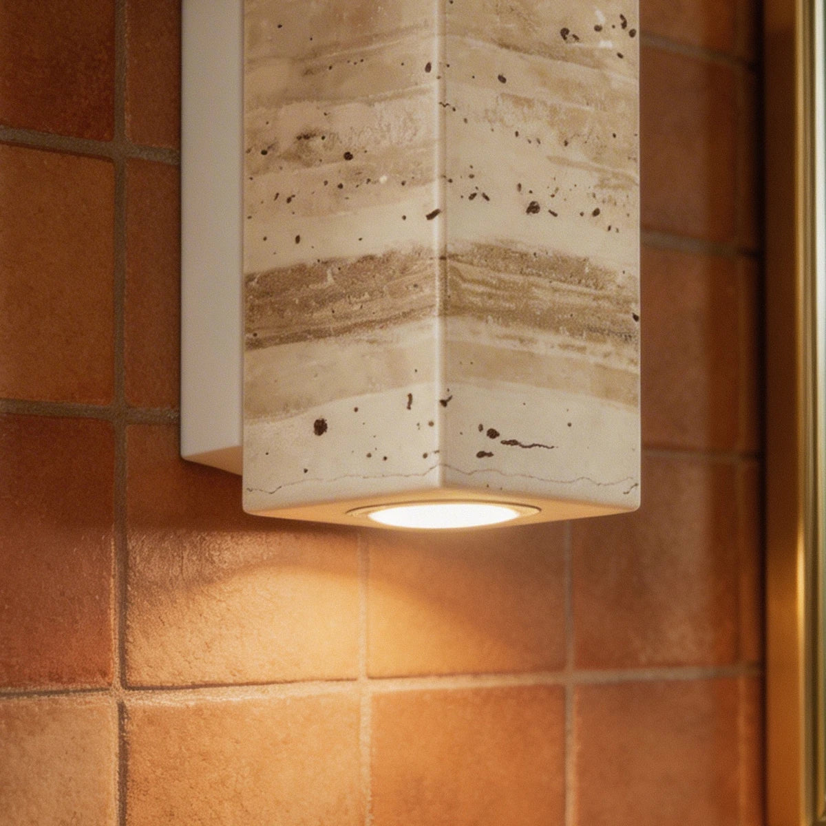 A tight detail of the Clérachic wall lamp's stone corner and downlight against terracotta tile.
