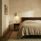 A Clérachic wall lamp lights a bedside corner above a dark wood nightstand with fresh flowers.