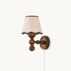 Clérachic wall light on a white backdrop, with a walnut-toned turned wood arm, a scalloped fabric shade and a pull chain.