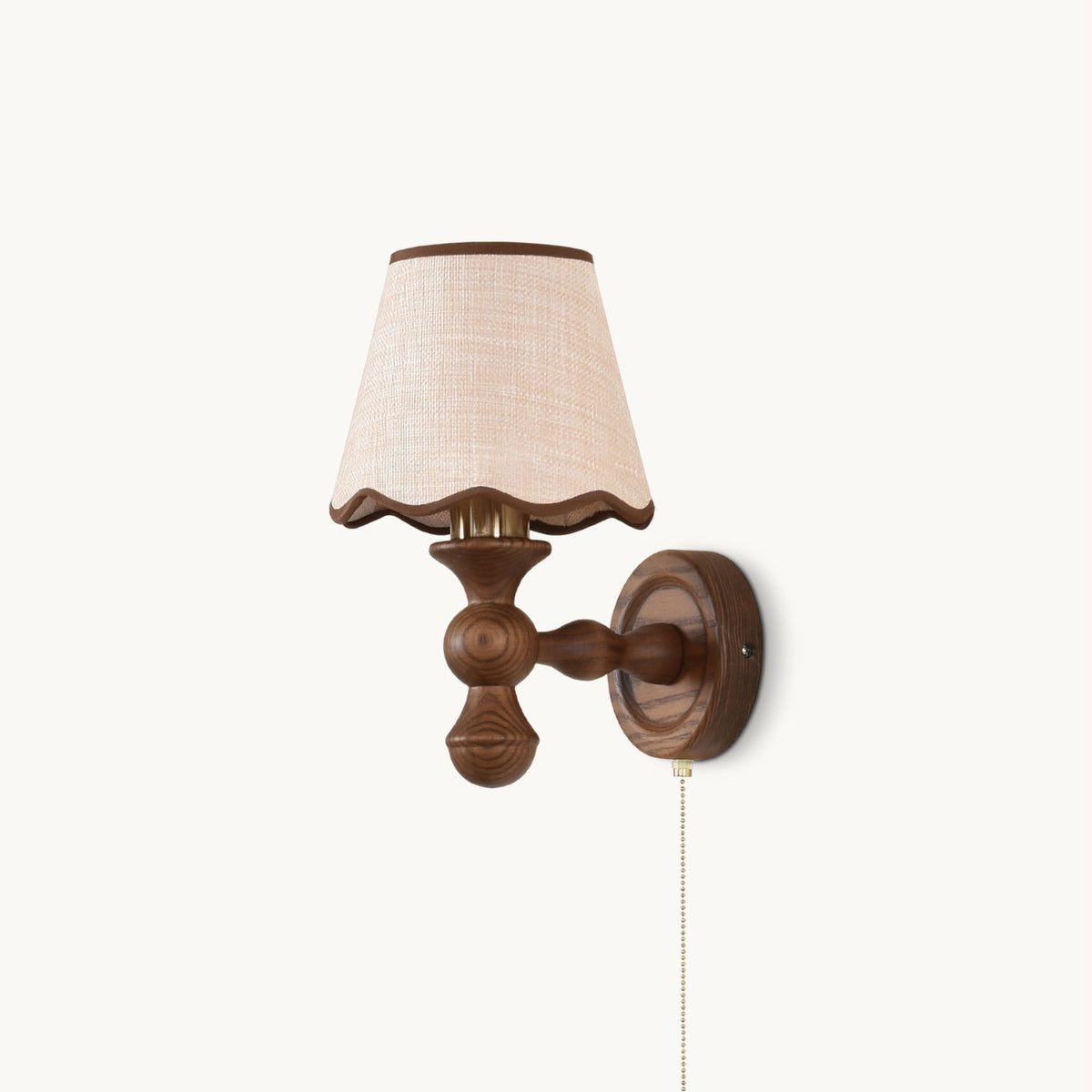 Clérachic wall light on a white backdrop, with a walnut-toned turned wood arm, a scalloped fabric shade and a pull chain.