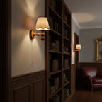 This Clérachic wall light glows beside a tall bookcase in a dark wood-panelled hallway, with a leather armchair beyond.