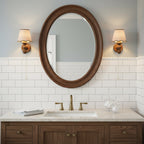 Two Clérachic wall lights on either side of an oval wooden mirror above a basin, with white tiles behind.