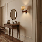 A Clérachic walnut wall light in a hallway beside a round mirror, above a slim wooden console table.