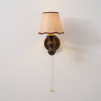 Front view of this Clérachic wall light, with a woven-look shade edged in brown and a walnut-toned turned base.
