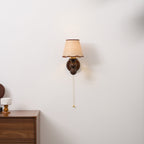 A Clérachic walnut wall light on a pale wall above a wooden chest of drawers, with a small cup beside it.