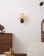 This Clérachic wall light on a white wall is set back in a room with a chest of drawers and a cream chair below.