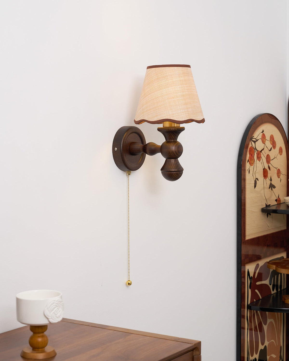 Clérachic walnut wall light beside an arched painted screen, with a white cup on a wooden stand below.