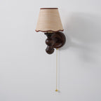 A Clérachic walnut wall light on a pale grey wall, shown from a slight angle with a long pull chain.