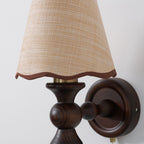 Close detail of the woven shade, brown scalloped trim and turned walnut base of this Clérachic wall light.