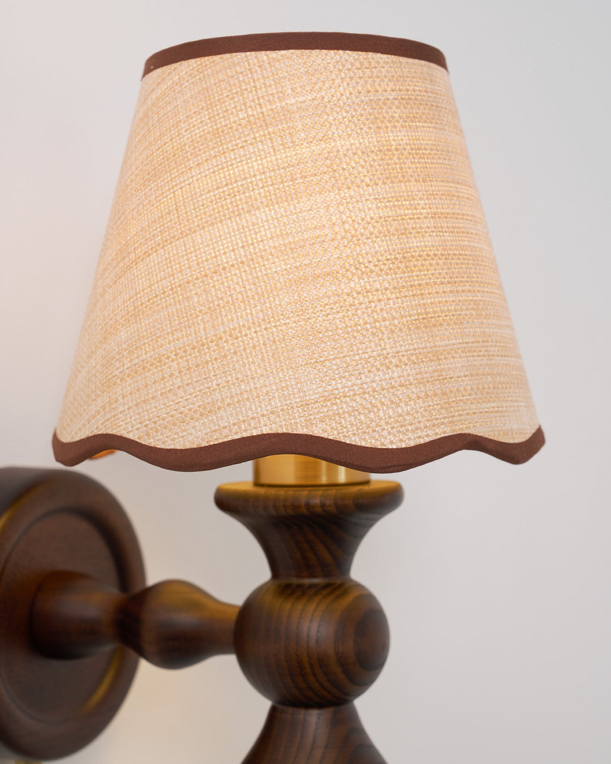 Close view of the brass-toned fitting under the shade and the turned walnut arm on this Clérachic wall light.