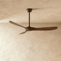 Clérachic three-blade ceiling fan with dark wood blades and a dark body on a downrod, hung against a limewashed studio ceiling