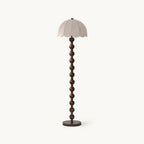 Floor lamp with a scalloped dome shade in beige fabric, a stem of stacked walnut balls and a round dark base, on white; a Clérachic design.