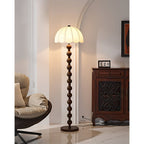 Warm light glows through the pleated shade, with a wooden cabinet and a cream lounge chair behind; a Clérachic floor lamp.
