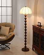 Tall view of the lit lamp between a cushioned chair and an ornate wood cabinet, in a room with an arched wall; from Clérachic.