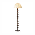 Straight-on view of the lit shade, the stacked walnut balls and the round base on a pale background; a Clérachic floor lamp.