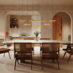 Row of Clérachic wooden leaf pendants above a round dining table with rattan chairs, in a room with arched openings.