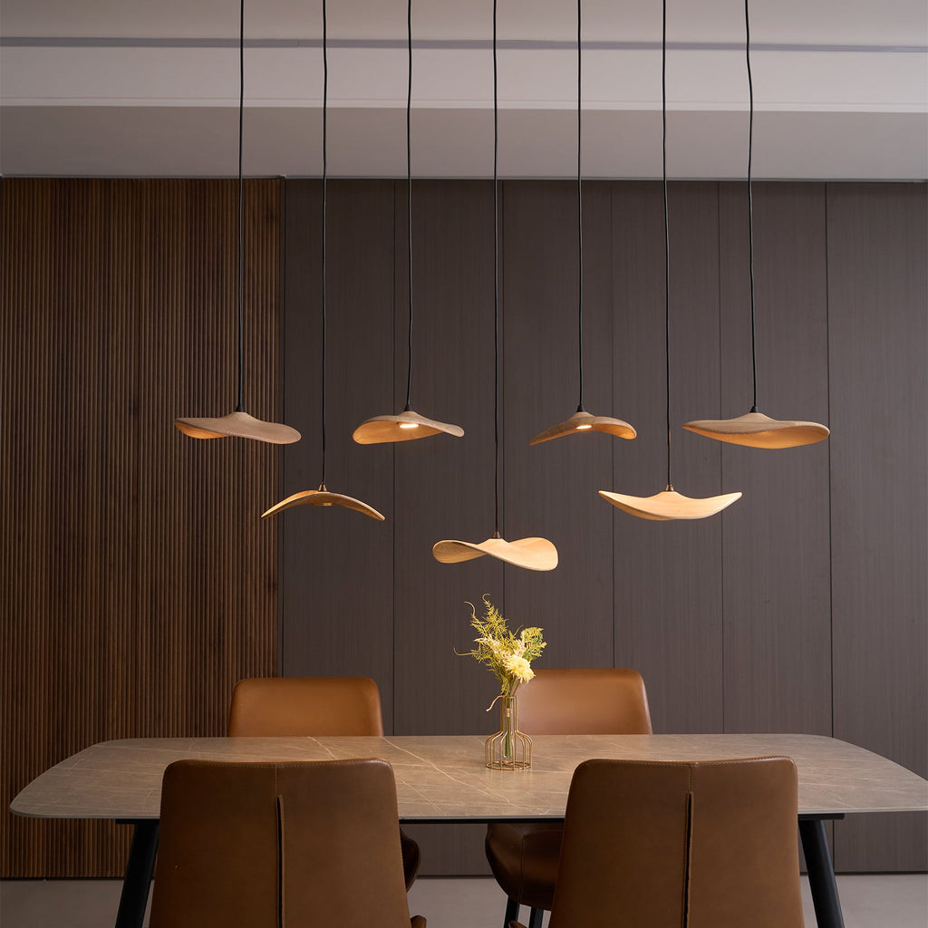 Seven Clérachic wooden leaf pendants lit at varied heights against a dark wood-panelled wall, above a dining table.