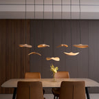Seven Clérachic wooden leaf pendants lit at varied heights against a dark wood-panelled wall, above a dining table.