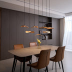 Clérachic leaf pendants glowing at different heights in a dining room with brown leather chairs and a built-in shelf.