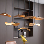 Close view of Clérachic wooden leaf pendants, lit from beneath, with a vase of yellow flowers and a shelf behind.
