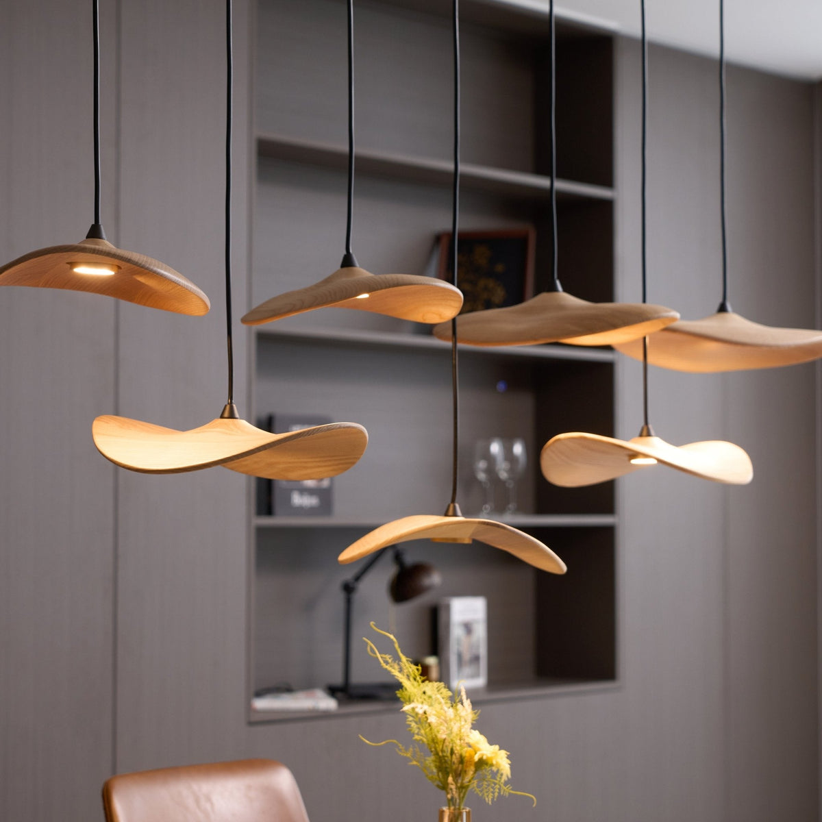 Close view of Clérachic wooden leaf pendants, lit from beneath, with a vase of yellow flowers and a shelf behind.