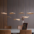 Unlit Clérachic wooden leaf pendants at varied heights over a stone table, with a framed gold botanical print.