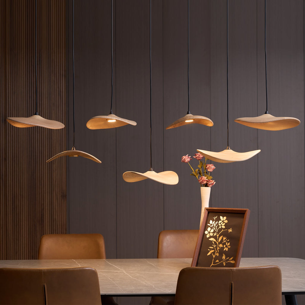 Lit Clérachic wooden leaf pendants over a stone dining table, with a vase of pink flowers and a framed print.