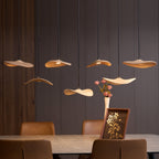 Lit Clérachic wooden leaf pendants over a stone dining table, with a vase of pink flowers and a framed print.