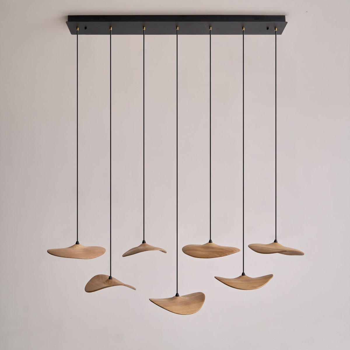 Seven Clérachic leaf pendants hanging from a long black rectangular canopy, on a plain pale background.