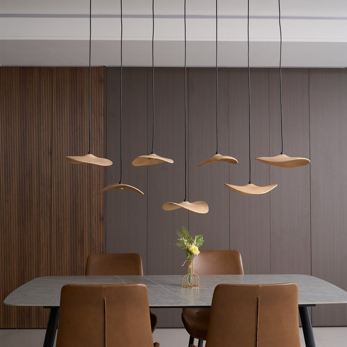Clérachic leaf pendants lit in staggered rows against a ribbed timber wall, above a table with a flower vase.