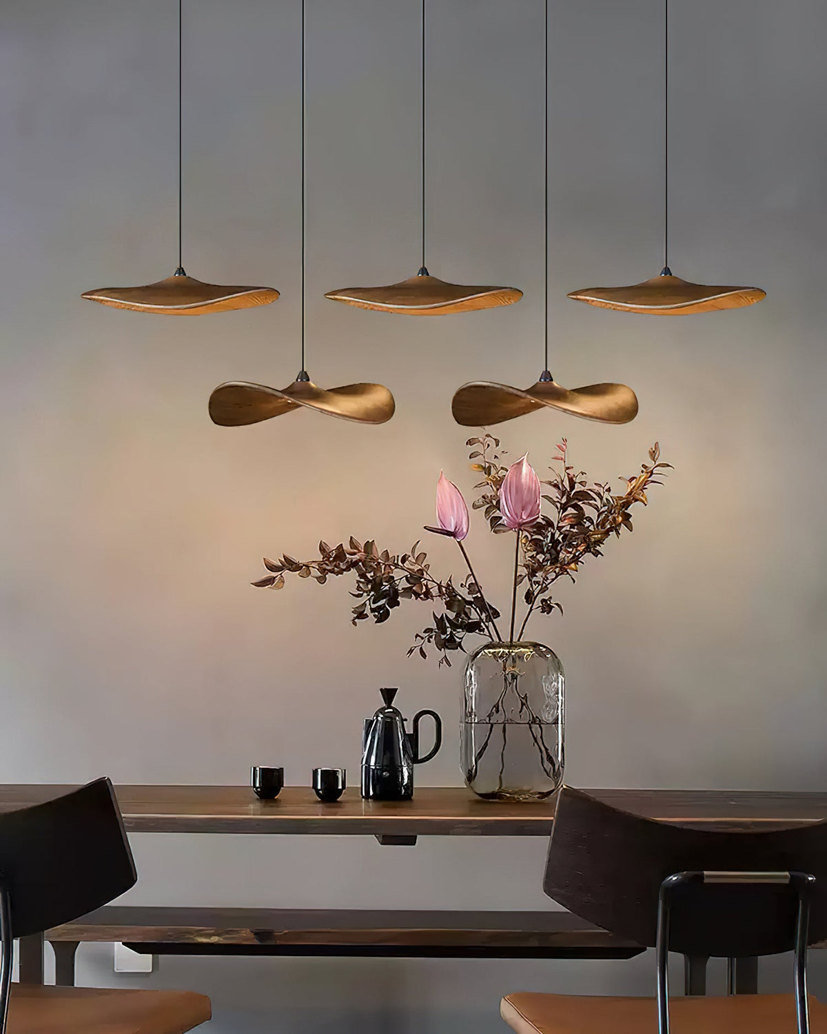Five Clérachic leaf pendants in two rows over a dark wood table, with a glass vase of pink blooms and a kettle.