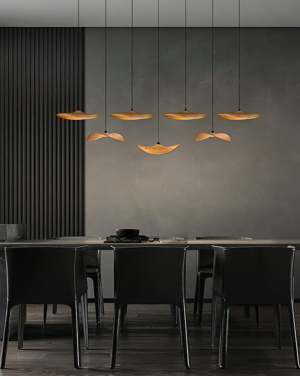 Seven Clérachic wooden leaf pendants over a dark dining area with black chairs and a charcoal wall panel.