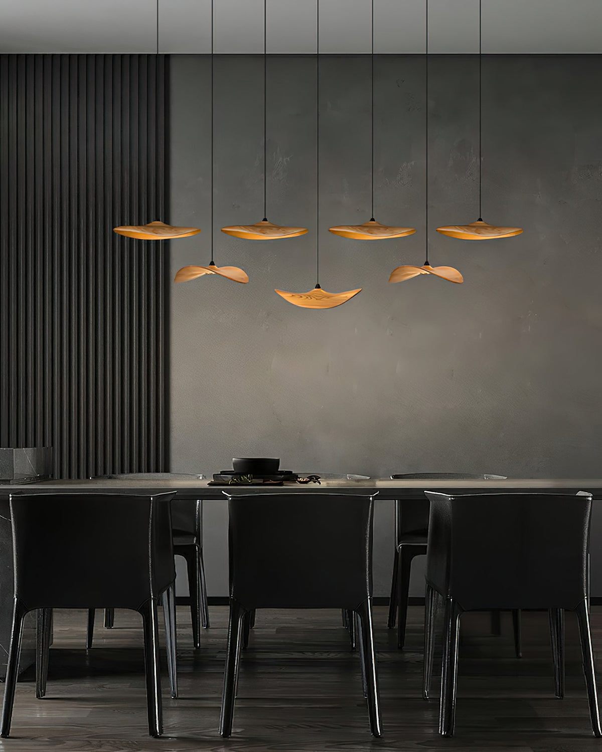 Seven Clérachic wooden leaf pendants over a dark dining area with black chairs and a charcoal wall panel.