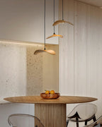 Three Clérachic wooden leaf pendants over a round pedestal table with a bowl of fruit, beside a wood-slat wall.