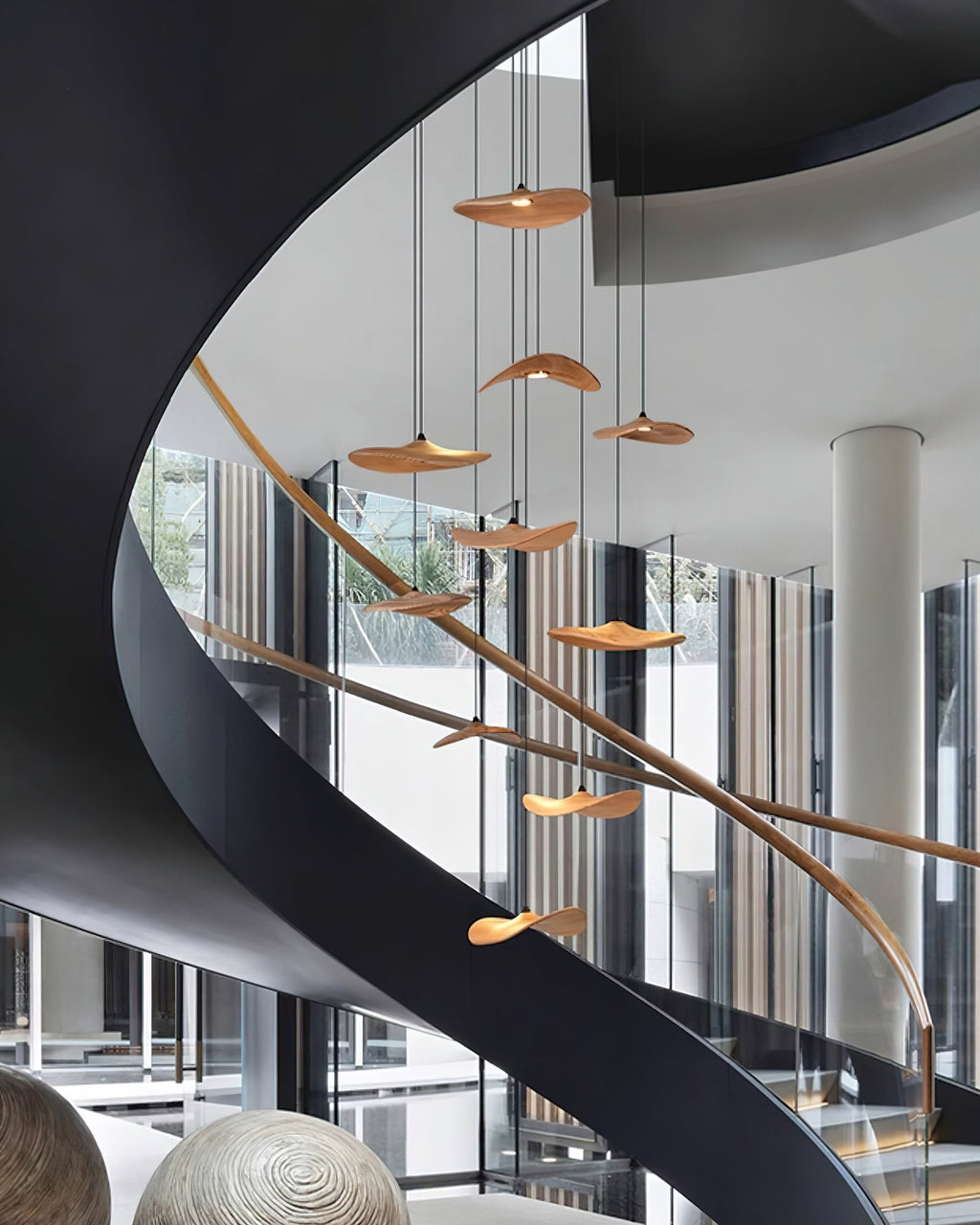 Clérachic leaf pendants hung at many heights alongside a sweeping black spiral staircase with a timber handrail.