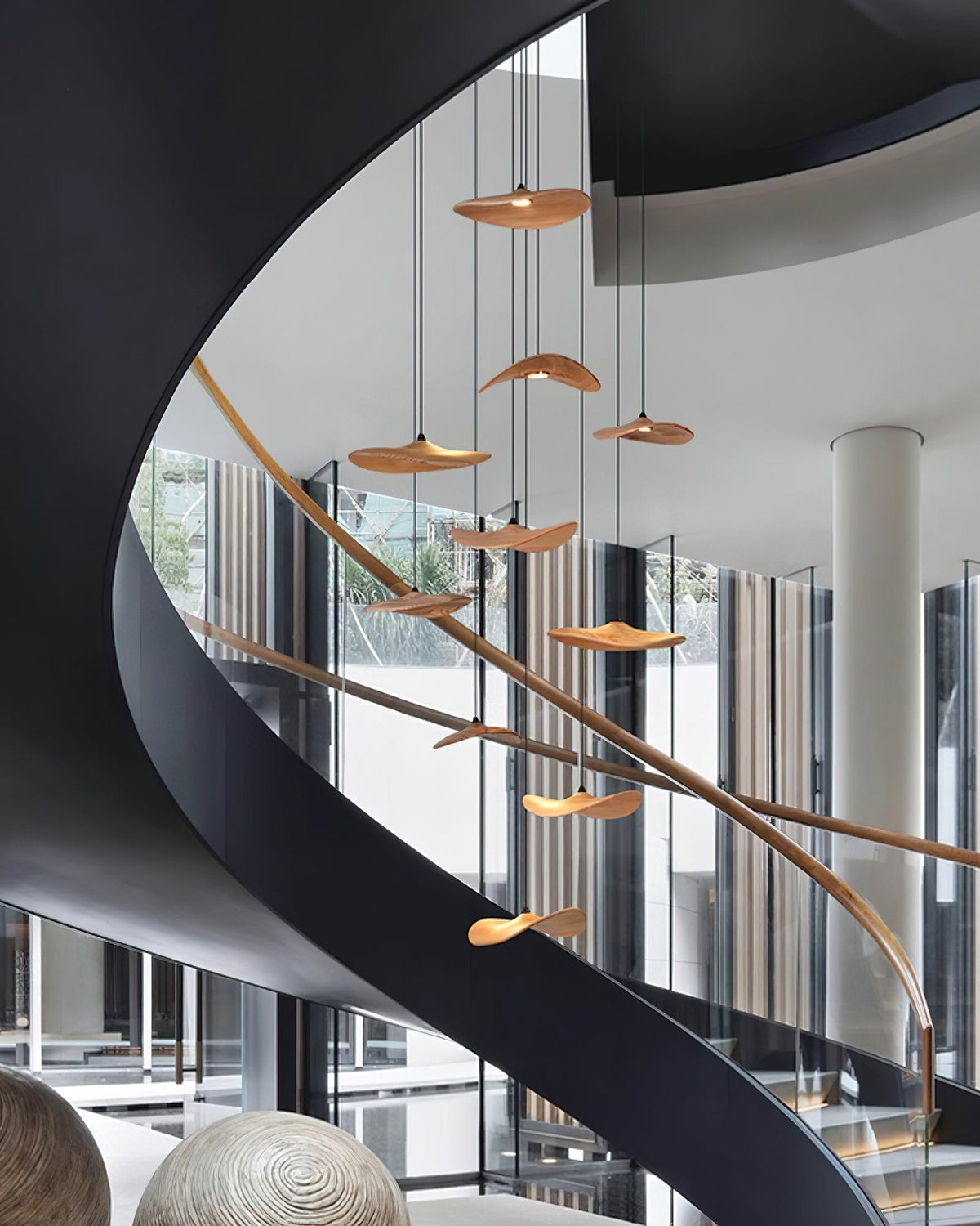 Clérachic leaf pendants hung at many heights alongside a sweeping black spiral staircase with a timber handrail.