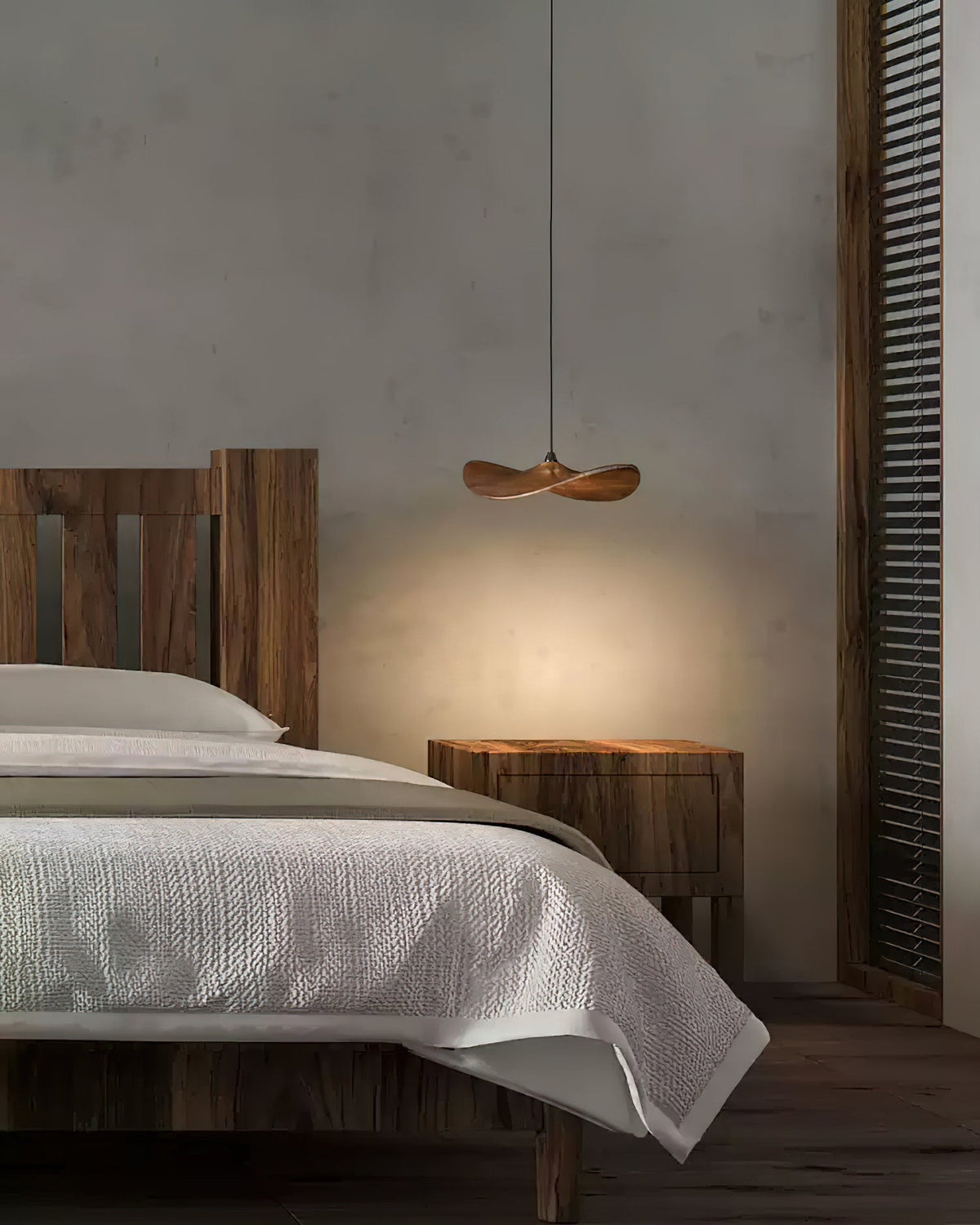 A single Clérachic wooden leaf pendant glowing beside a bed with white linen and a rustic wooden headboard.
