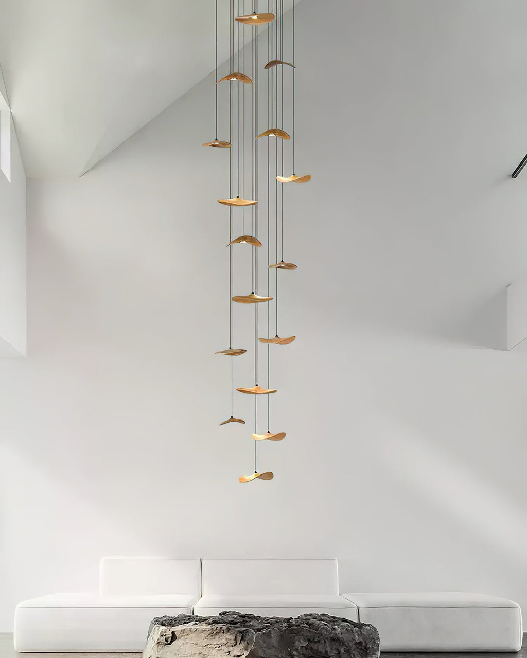 Long column of Clérachic leaf pendants descending through a tall white stairwell, above a low white sofa.