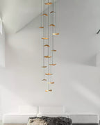 Long column of Clérachic leaf pendants descending through a tall white stairwell, above a low white sofa.